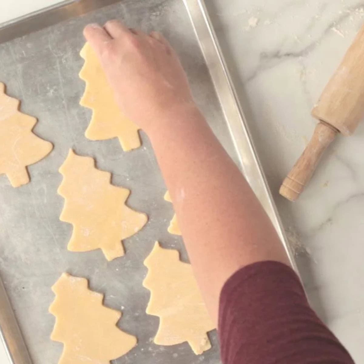 A hand lays cookie dough cut-outs on a cookie sheet to be baked.