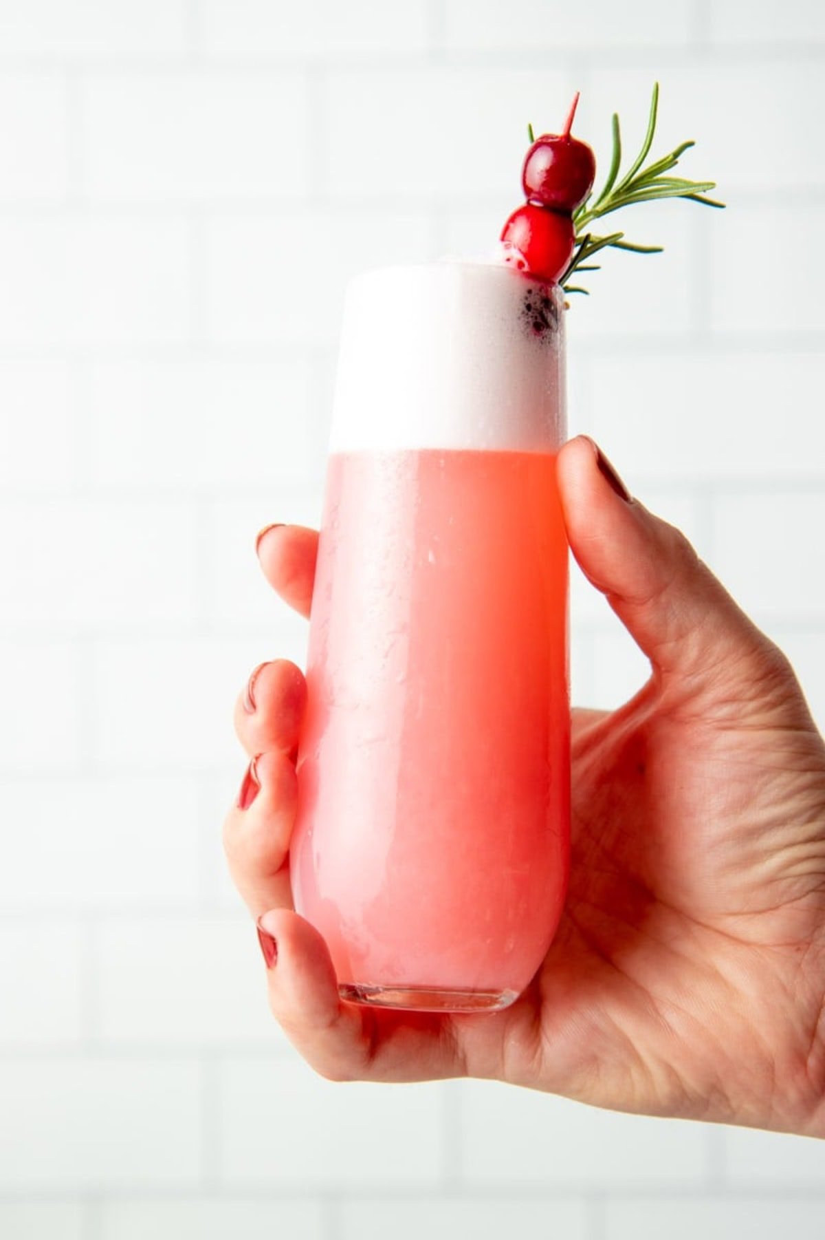 A hand holds out a cranberry gin fizz in a tall, narrow glass.