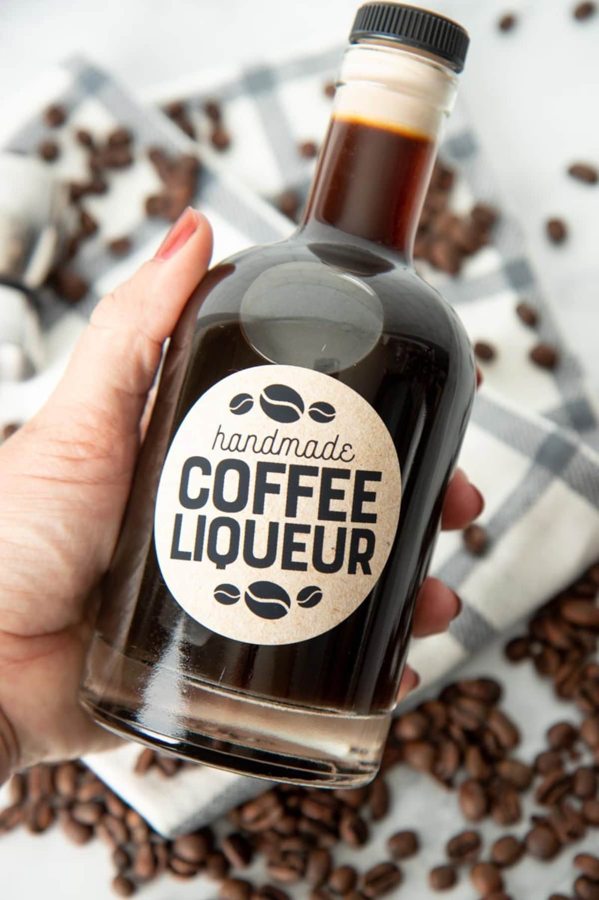 A hand holds up a labeled bottle of homemade coffee liqueur.