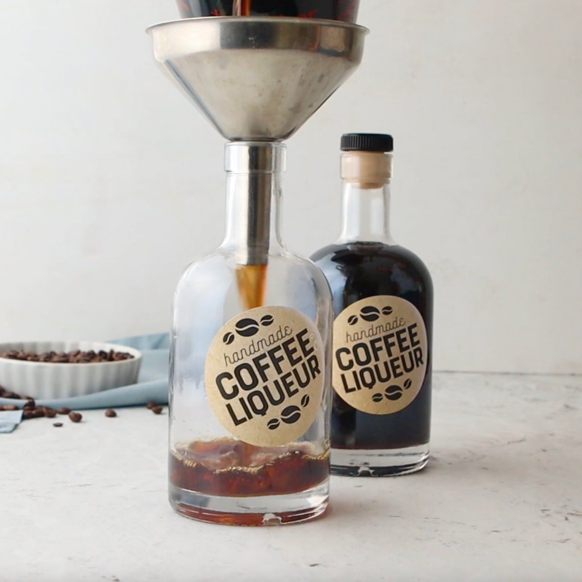 Homemade coffee liqueur pours into a bottle through a metal funnel.