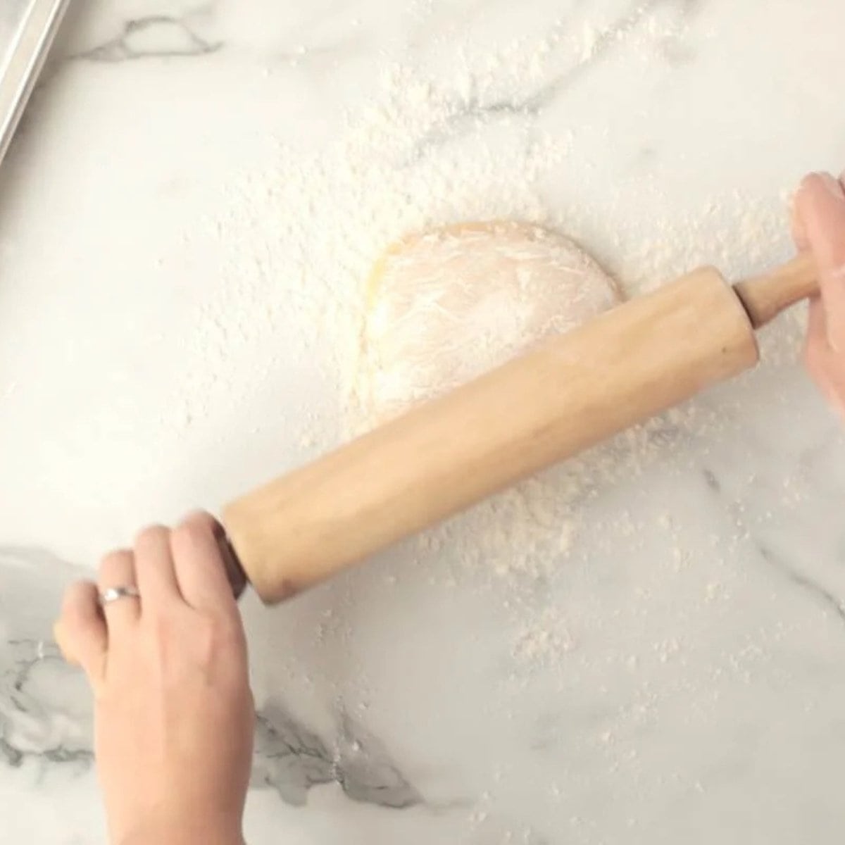 A rolling pin rolls out cookie dough on a floured surface.