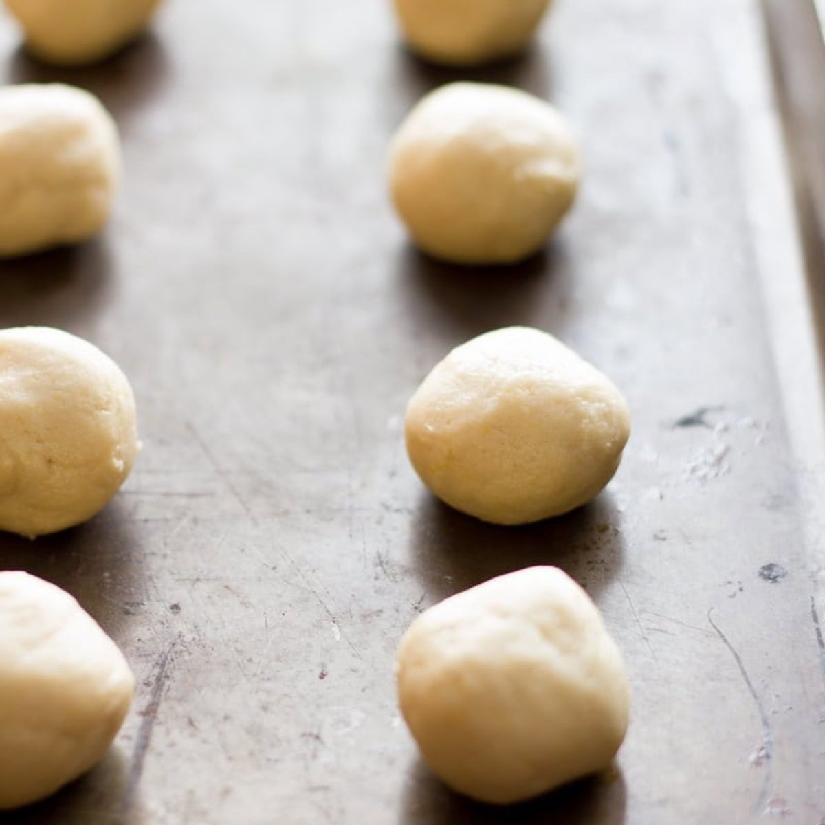 Balls of dough for lemon crinkle cookies on a baking sheet.