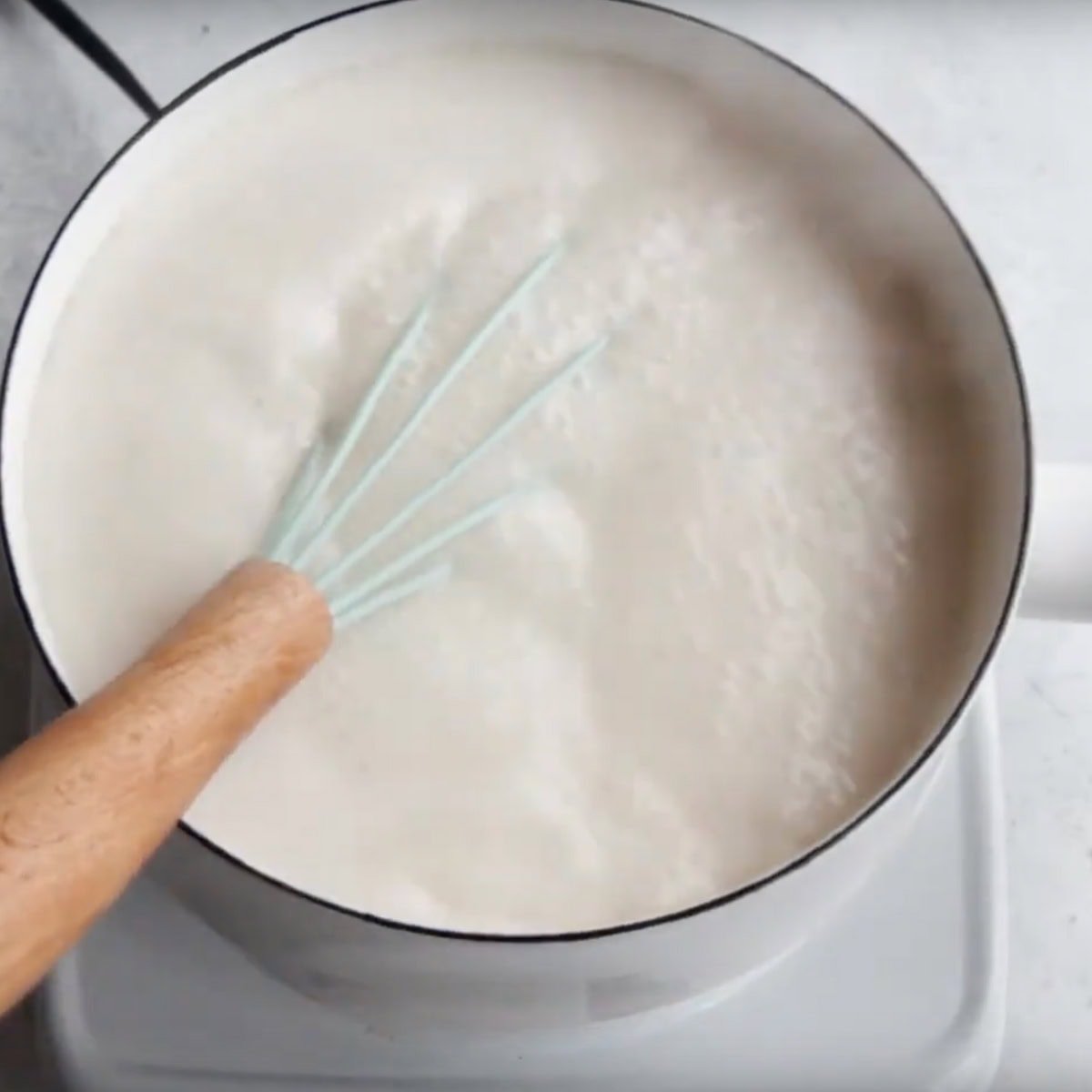 A whisk in a pot of bubbling hot milk.