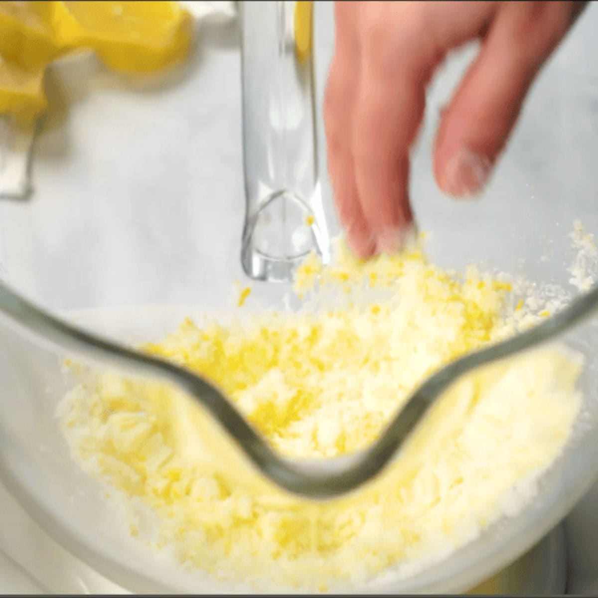 Hands make lemon sugar in a glass mixing bowl.