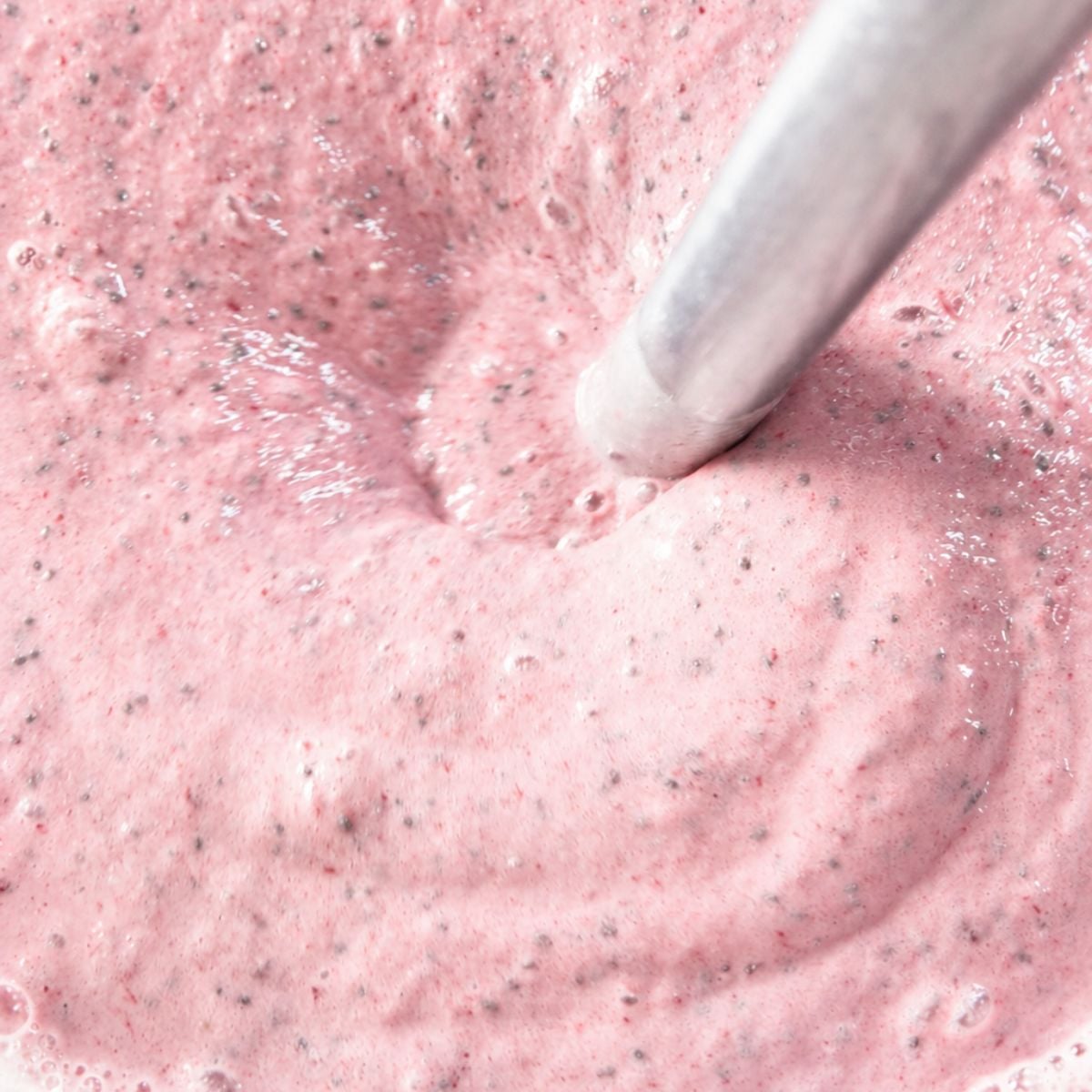 Close-up of creamy pink strawberry chia pudding being stirred in a bowl showing the thick texture and chia seeds