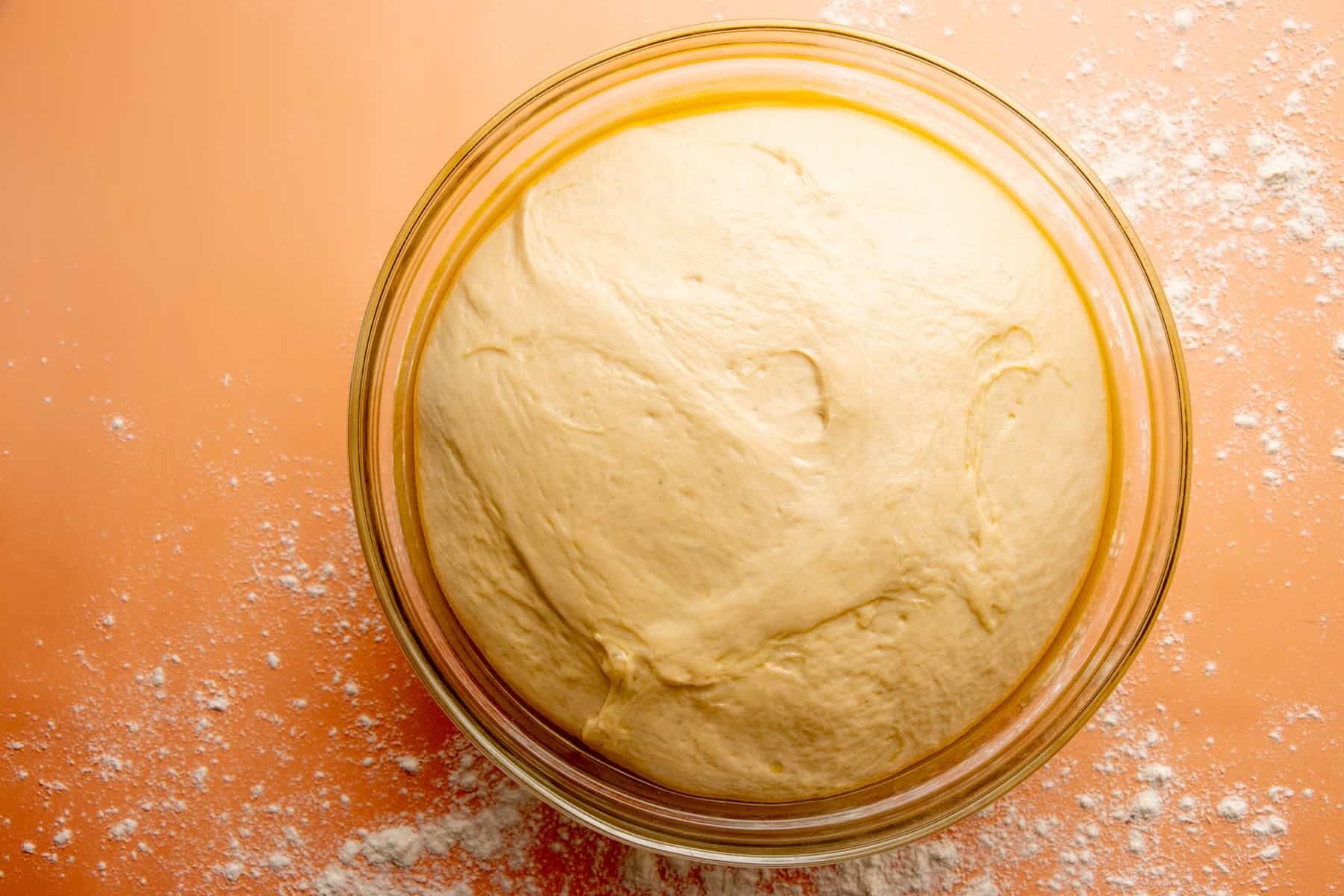 Risen dough sits in a glass bowl.